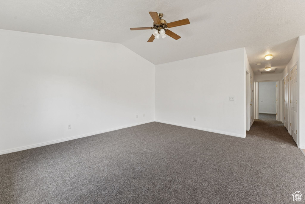 Spare room featuring dark carpet, vaulted ceiling, and ceiling fan