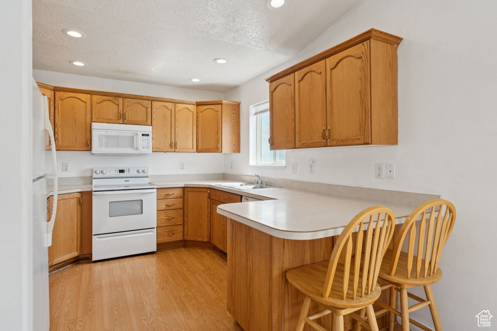 Kitchen featuring white appliances, a peninsula, recessed lighting, light wood-style floors, and light countertops