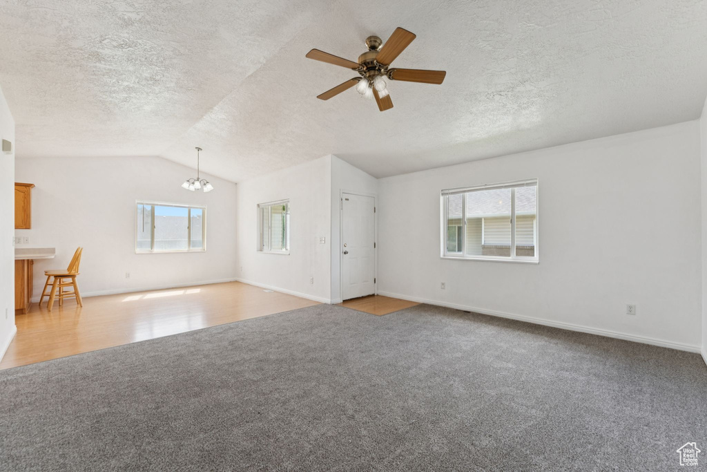 Unfurnished living room with light carpet, lofted ceiling, a chandelier, a ceiling fan, and a textured ceiling
