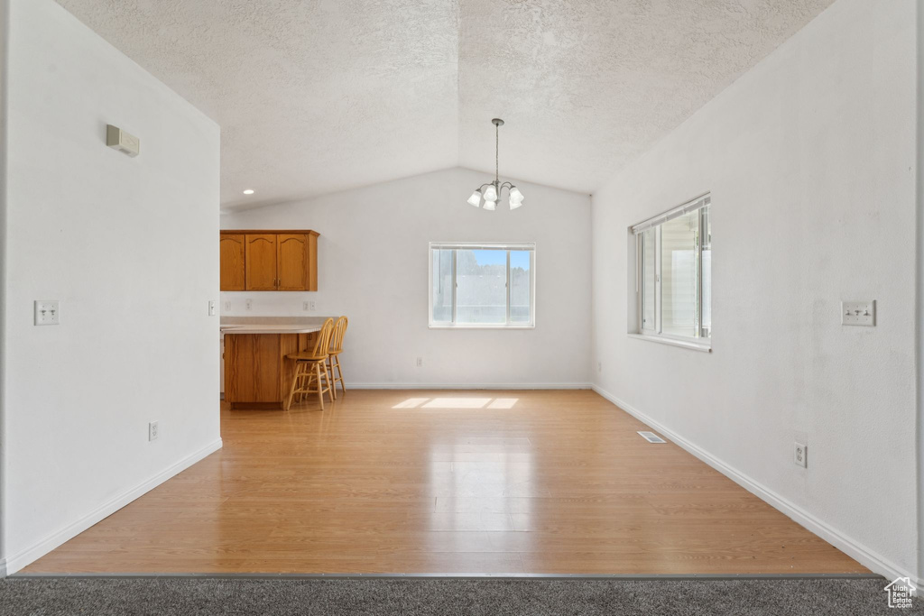 Unfurnished living room with lofted ceiling, light wood-style floors, a chandelier, and a textured ceiling