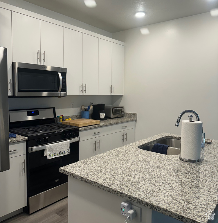 Kitchen featuring stainless steel appliances, wood finished floors, white cabinets, light stone counters, and recessed lighting