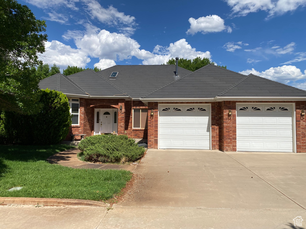 View of front of home featuring an attached garage, driveway, brick siding, and a front yard