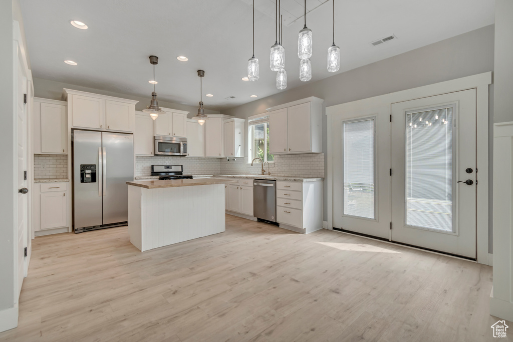 Kitchen with stainless steel appliances, tasteful backsplash, white cabinets, light wood finished floors, and recessed lighting