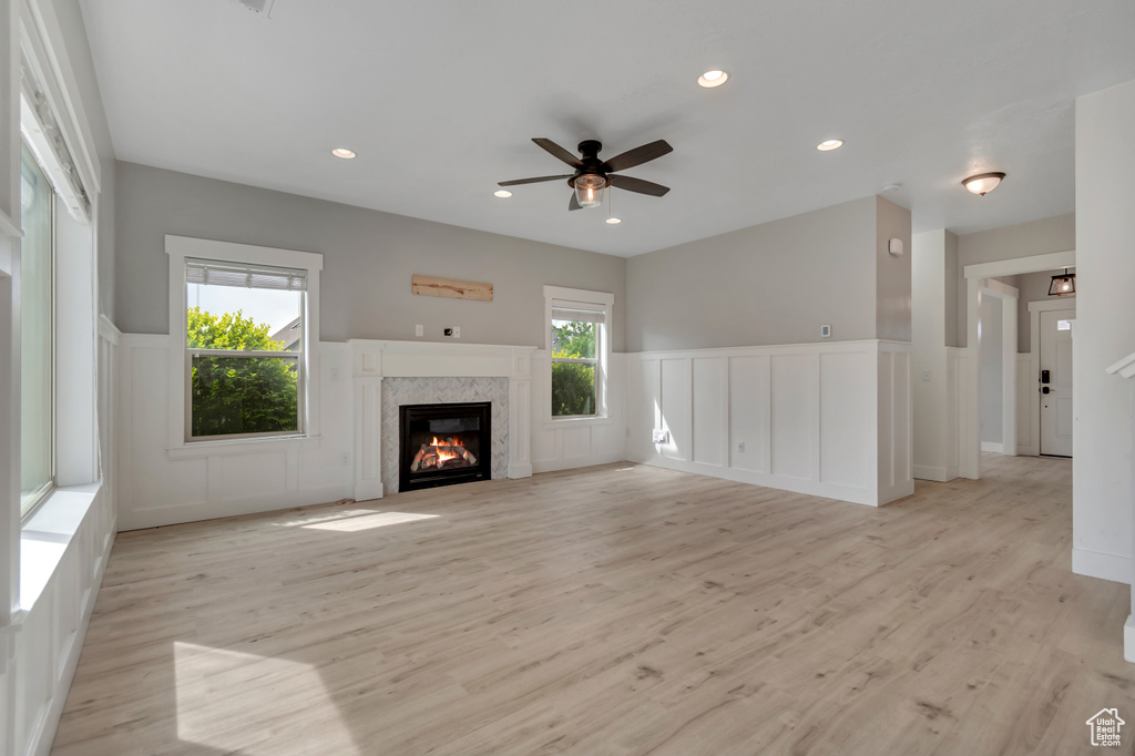 Unfurnished living room with a decorative wall, ceiling fan, light wood-style floors, a wainscoted wall, and a glass covered fireplace