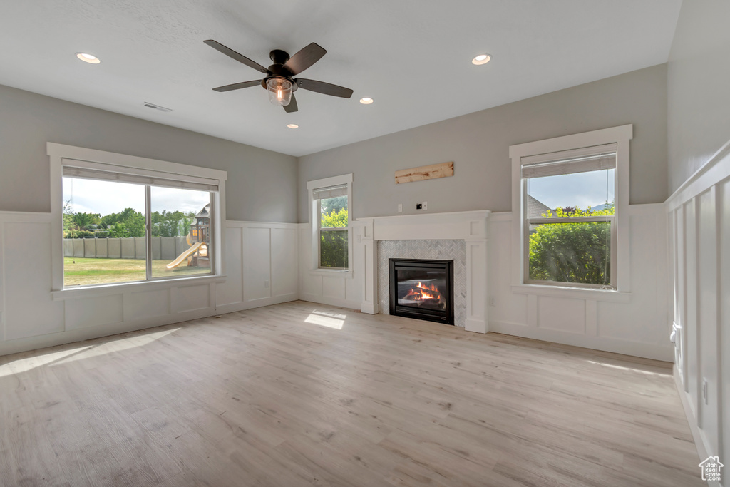 Unfurnished living room with a decorative wall, a wainscoted wall, light wood finished floors, a high end fireplace, and a ceiling fan