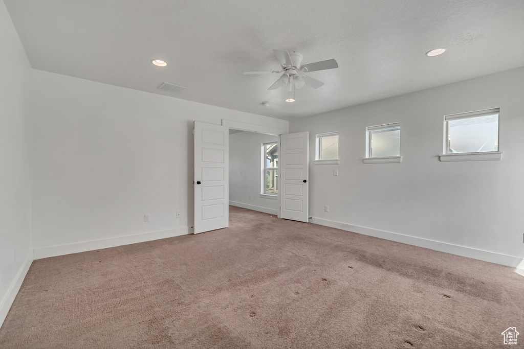 Carpeted empty room with a ceiling fan, plenty of natural light, and recessed lighting