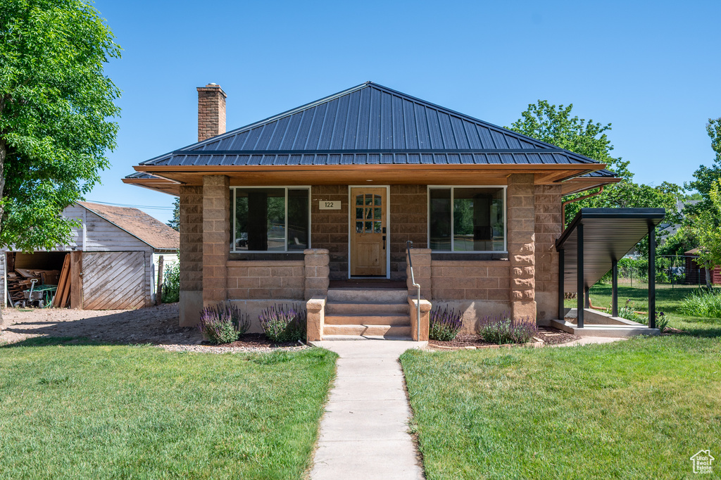 View of front facade featuring a chimney, a front lawn, and a metal roof
