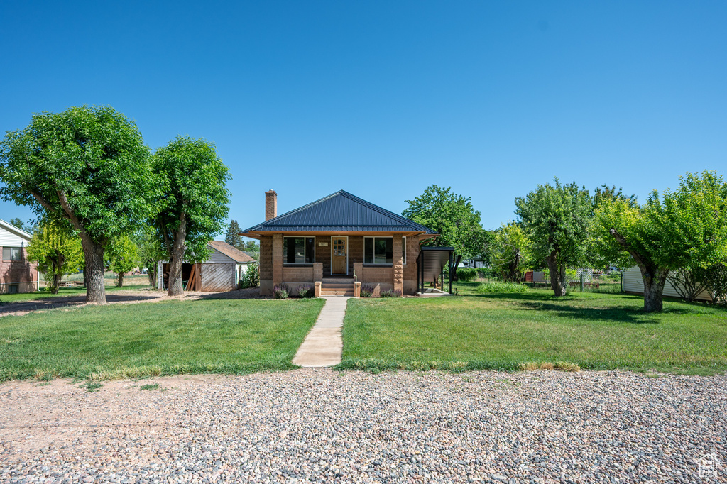 Bungalow-style home with a chimney, covered porch, and a front yard