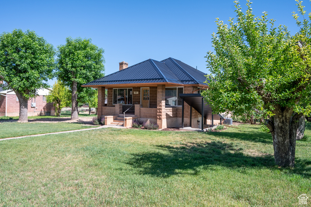 View of front of house with covered porch, a chimney, a front yard, a standing seam roof, and a metal roof