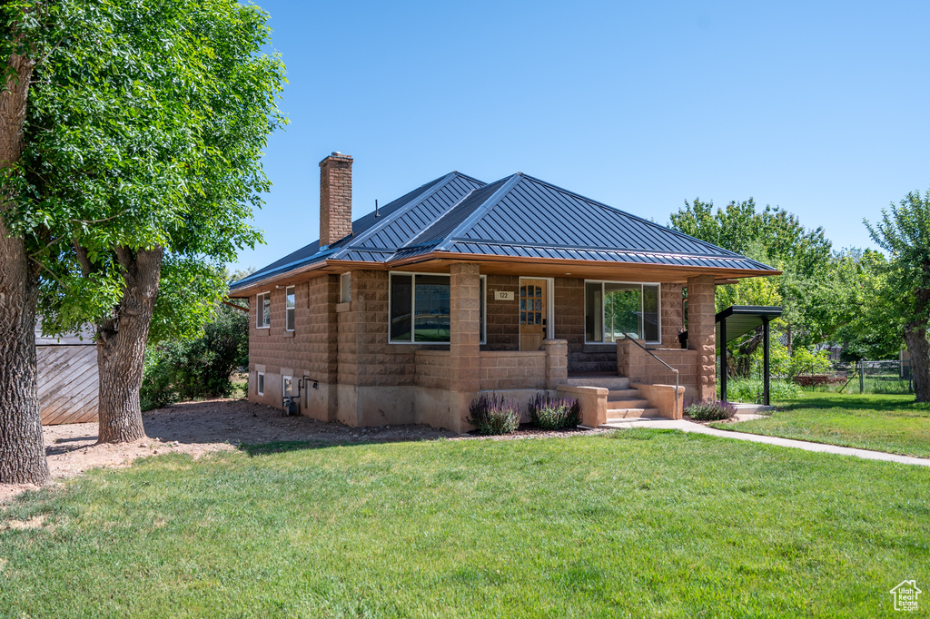View of front of property with covered porch, a standing seam roof, a chimney, a front yard, and a metal roof