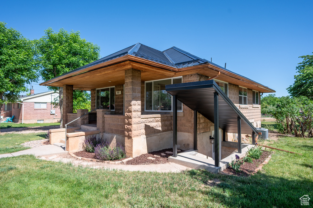 View of side of property featuring a yard, stone siding, and a metal roof