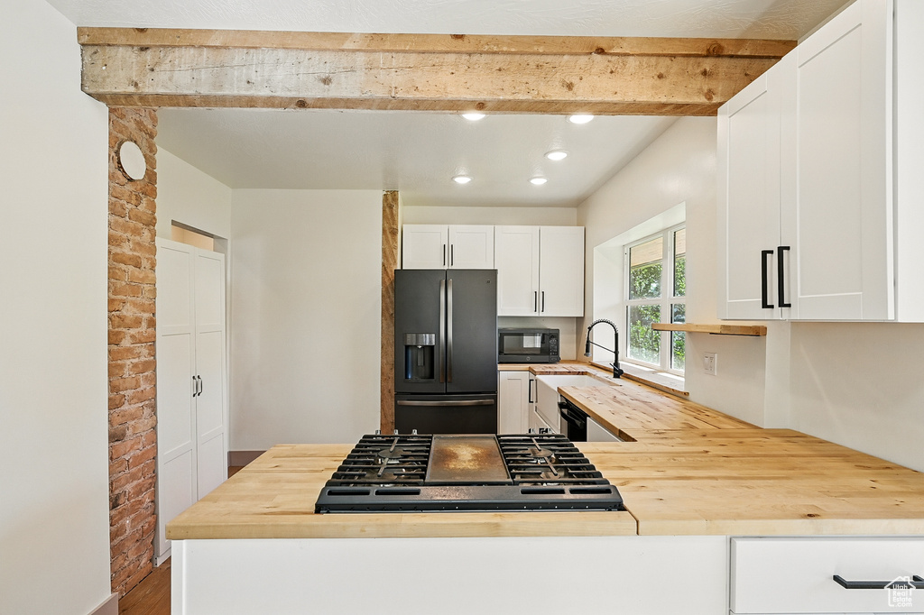 Kitchen with refrigerator with ice dispenser, butcher block counters, black microwave, beam ceiling, and cooktop