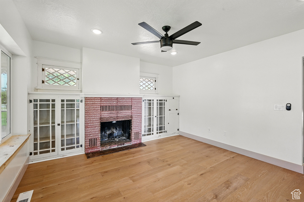 Unfurnished living room with wood finished floors, ceiling fan, and a brick fireplace