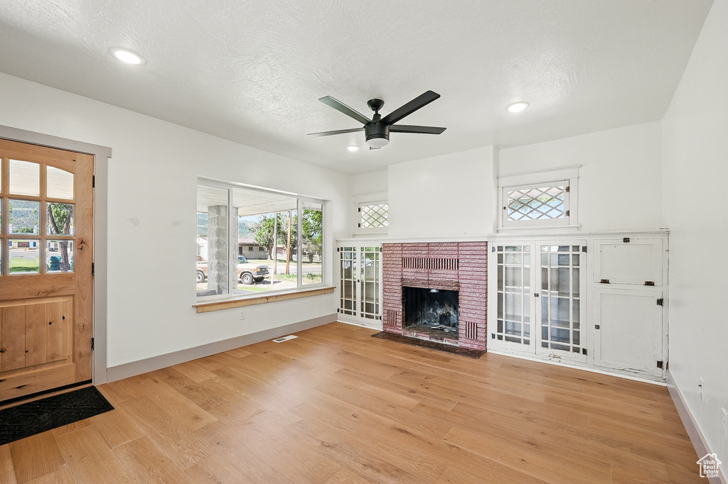 Unfurnished living room with wood finished floors, a ceiling fan, plenty of natural light, a fireplace, and recessed lighting