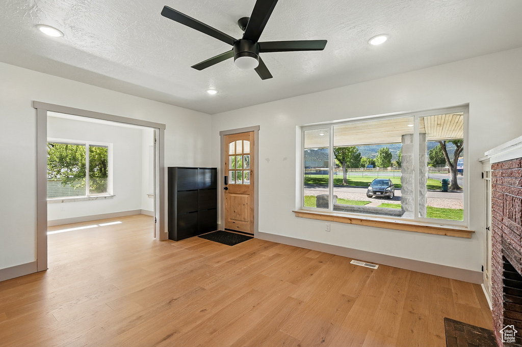 Unfurnished living room with a brick fireplace, light wood finished floors, a ceiling fan, recessed lighting, and a textured ceiling
