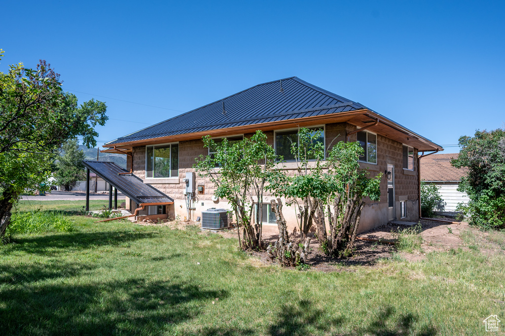 Back of property with a standing seam roof, a yard, a metal roof, and stone siding