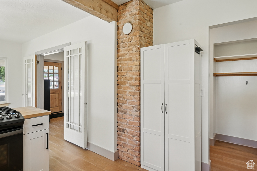 Kitchen featuring light wood-type flooring, black gas range, wood counters, and white cabinetry