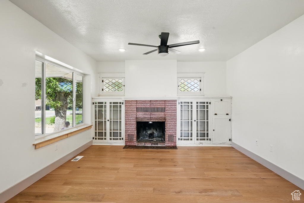 Unfurnished living room featuring a ceiling fan, a fireplace, healthy amount of natural light, and light wood-type flooring