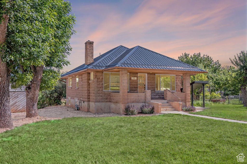 View of front of property with covered porch, a standing seam roof, a chimney, a front lawn, and a metal roof