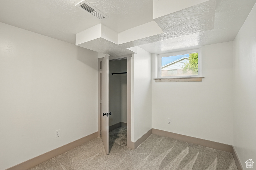 Unfurnished bedroom with light carpet, a closet, a walk in closet, and a textured ceiling