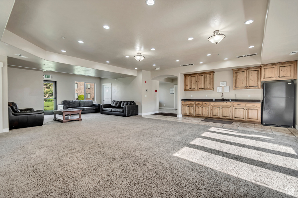 Living room featuring arched walkways, light carpet, recessed lighting, and bar with sink