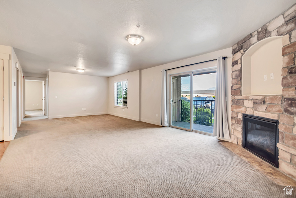 Unfurnished living room featuring a stone fireplace, light carpet, and plenty of natural light