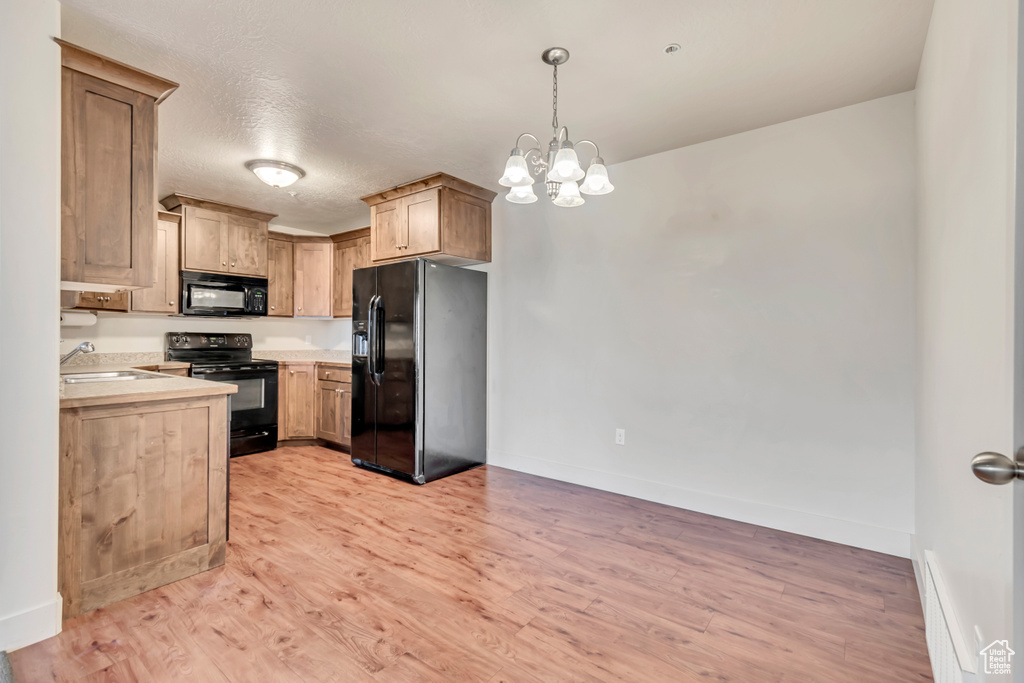 Kitchen featuring black appliances, light countertops, light wood-style flooring, pendant lighting, and a chandelier