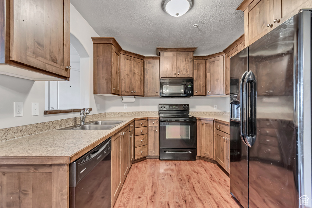 Kitchen featuring black appliances, light wood-style floors, light countertops, brown cabinets, and a textured ceiling
