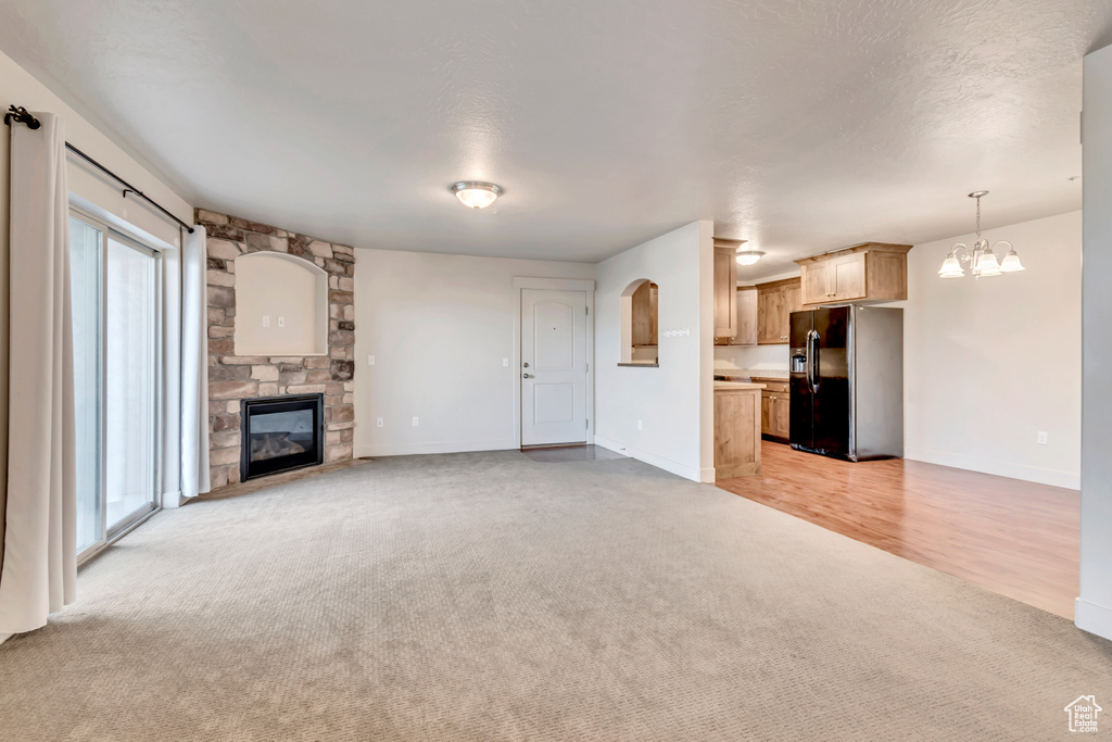 Unfurnished living room featuring light carpet, a fireplace, and a chandelier