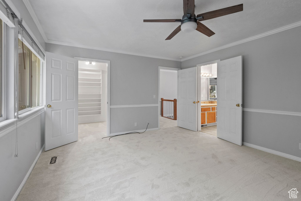 Unfurnished bedroom with carpet floors, a spacious closet, ornamental molding, a closet, and connected bathroom