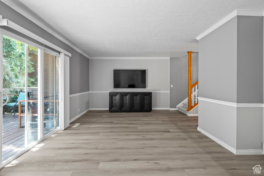 Unfurnished living room with wood finished floors, a textured ceiling, stairs, and ornamental molding