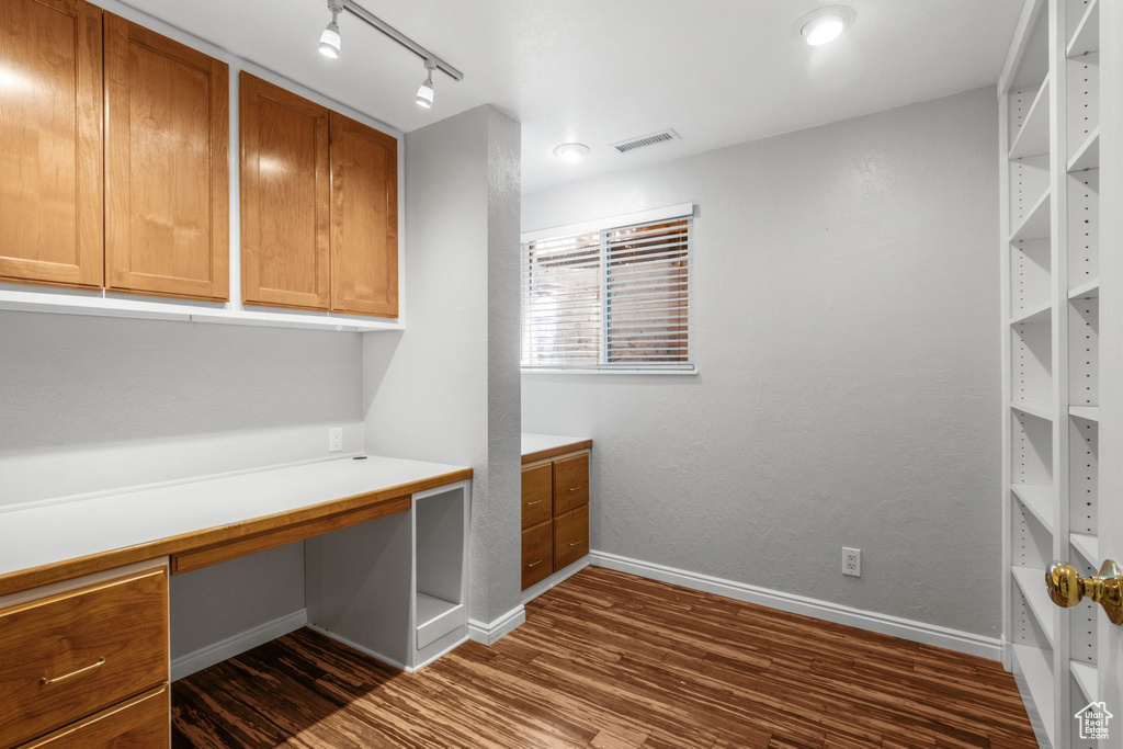 Unfurnished office featuring dark wood finished floors, built in desk, and track lighting