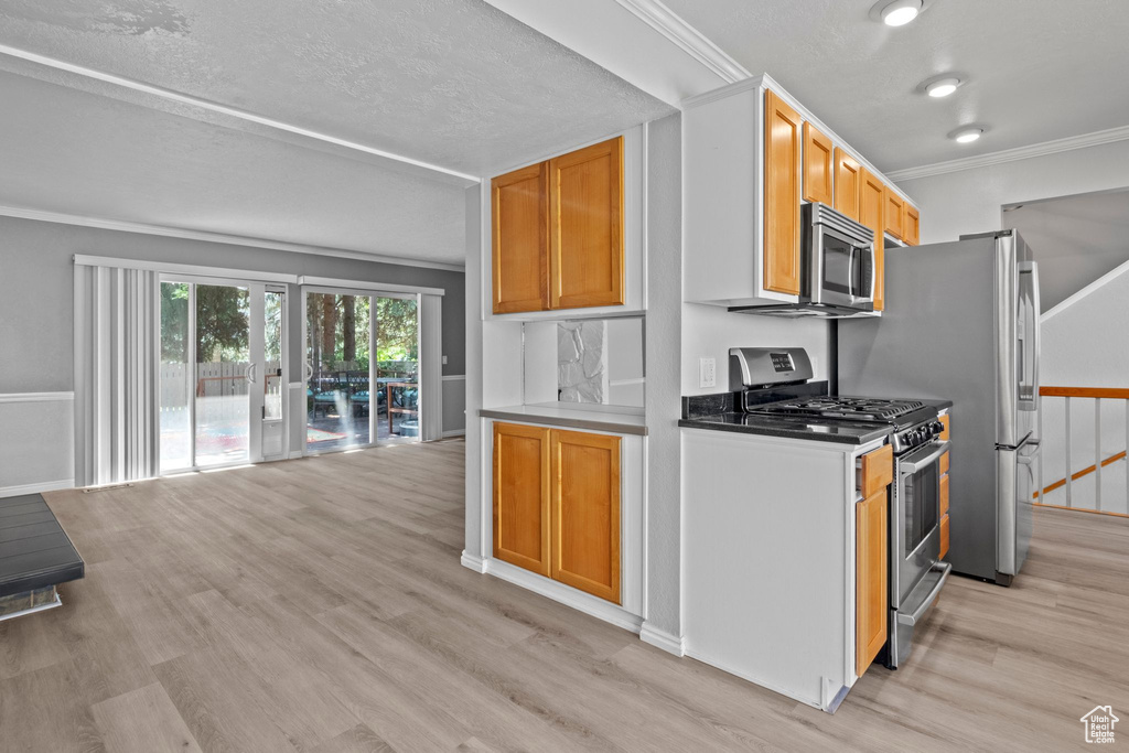 Kitchen with appliances with stainless steel finishes, light wood-type flooring, crown molding, and open floor plan