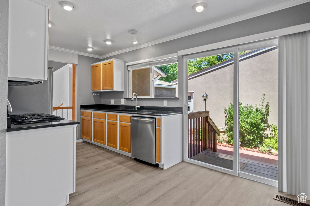 Kitchen featuring dishwasher, light wood finished floors, dark countertops, gas cooktop, and ornamental molding