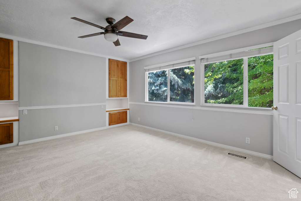 Spare room featuring a ceiling fan, light colored carpet, and crown molding