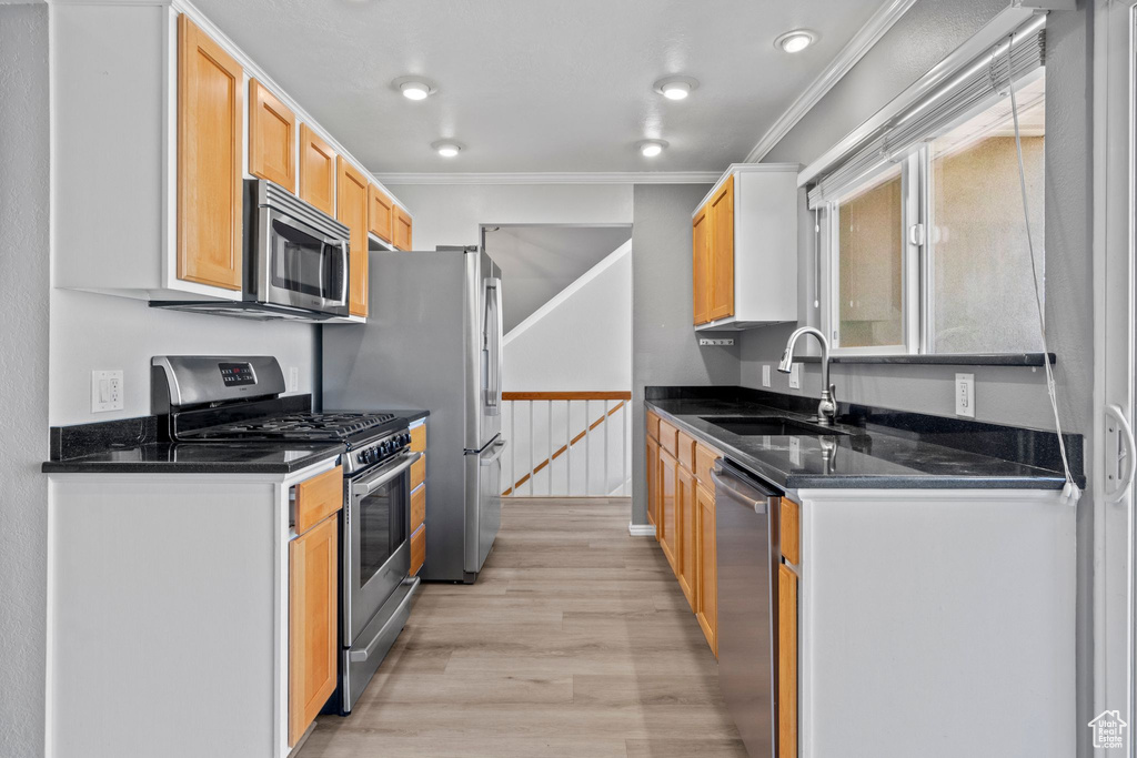 Kitchen with stainless steel appliances, ornamental molding, light wood-style flooring, and dark stone countertops