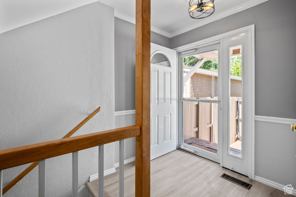 Doorway with wood finished floors, a chandelier, ornamental molding, and a textured wall