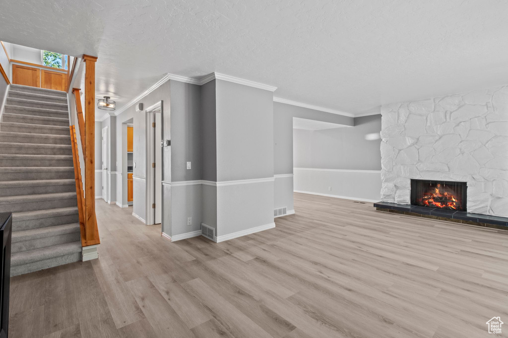Unfurnished living room with a fireplace, wood finished floors, crown molding, stairway, and a textured ceiling
