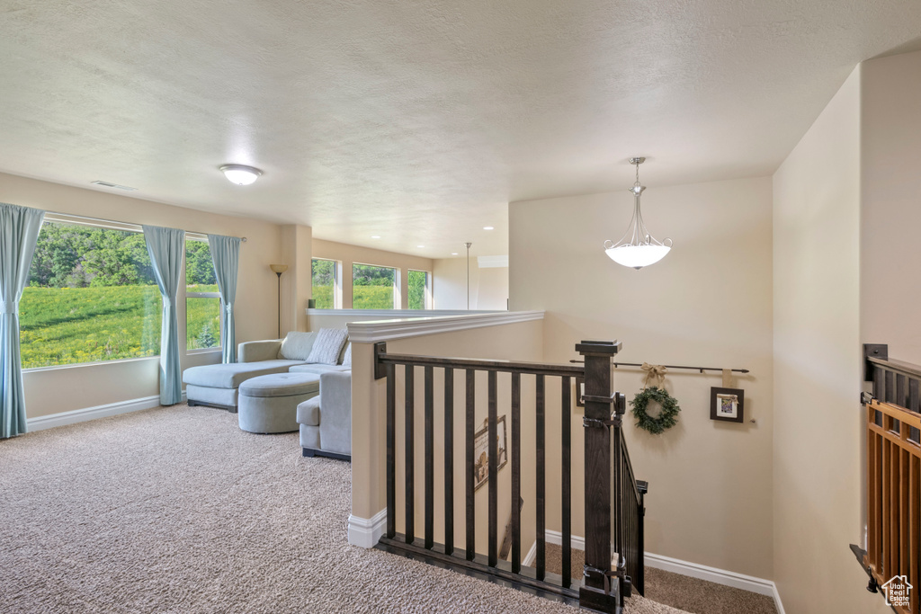 Hall featuring carpet, baseboards, an upstairs landing, and a textured ceiling