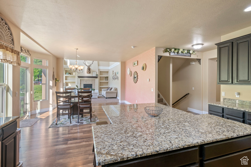 Kitchen featuring baseboards, open floor plan, wood finished floors, light stone countertops, and a textured ceiling