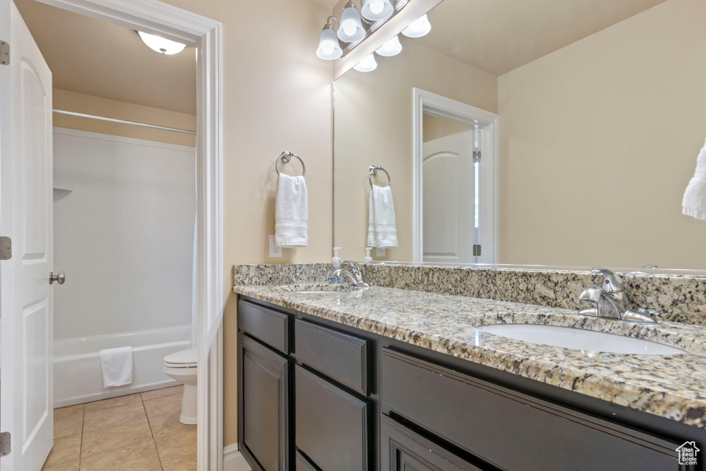 Full bathroom with double vanity, toilet, tile patterned floors, and shower / bath combination