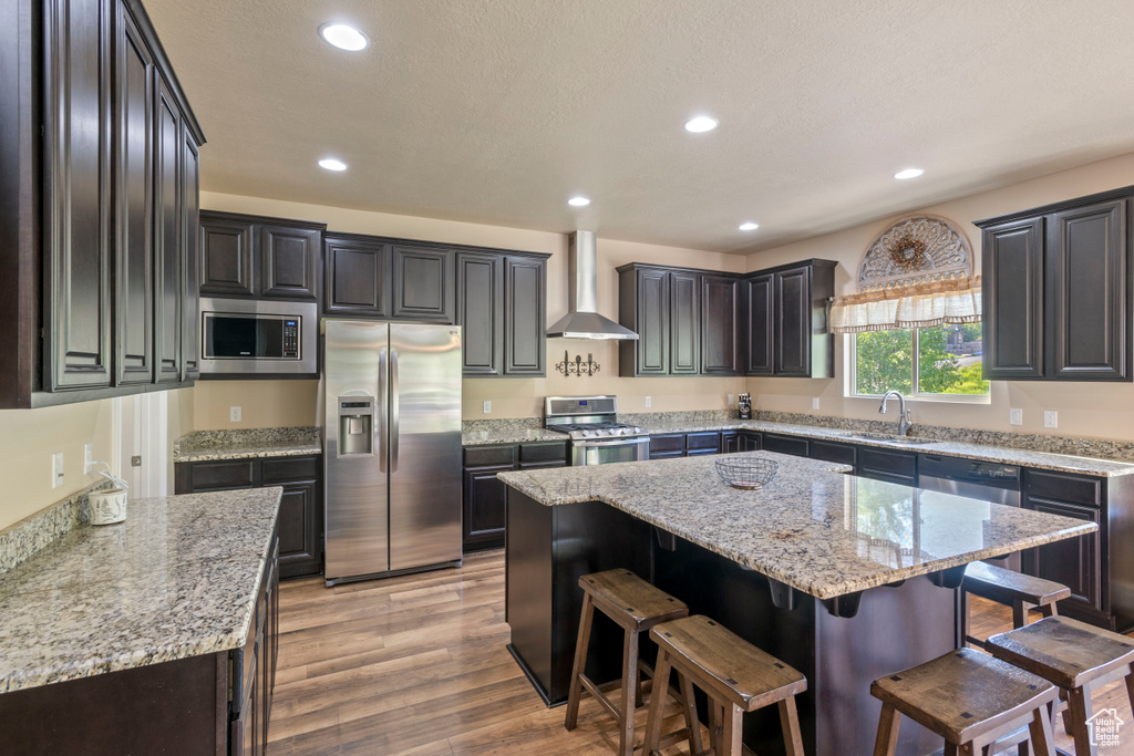 Kitchen featuring appliances with stainless steel finishes, wall chimney exhaust hood, a center island, recessed lighting, and a kitchen breakfast bar