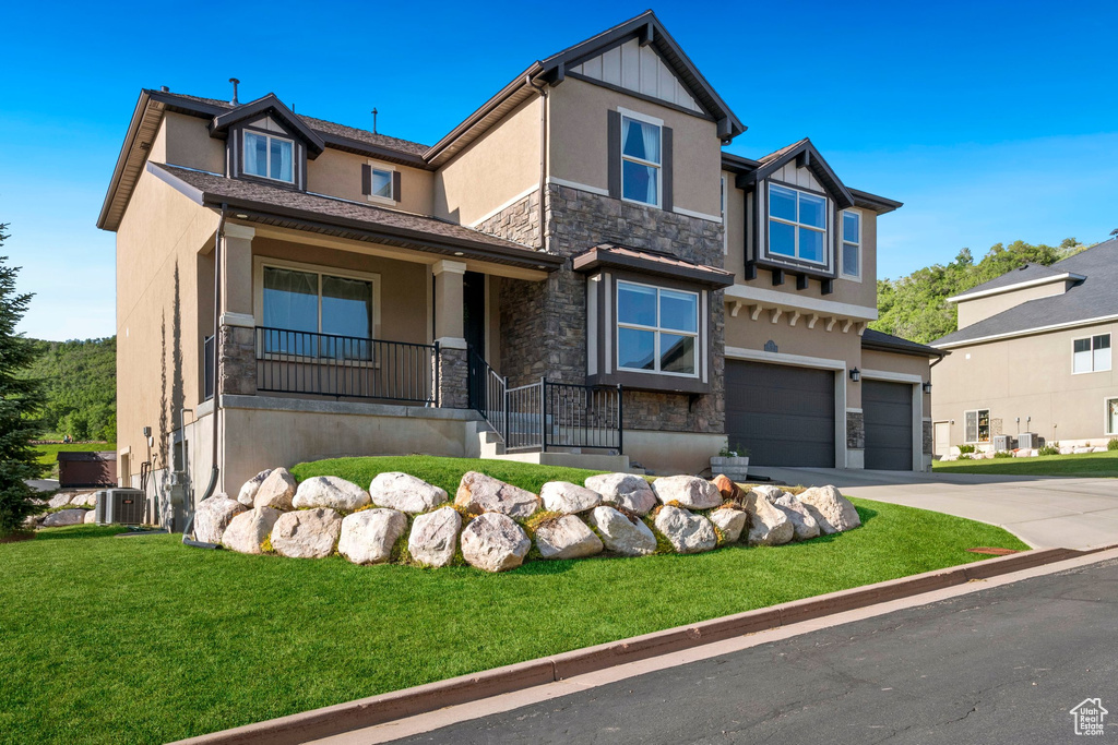 Craftsman house featuring stone siding, stucco siding, an attached garage, driveway, and a front lawn