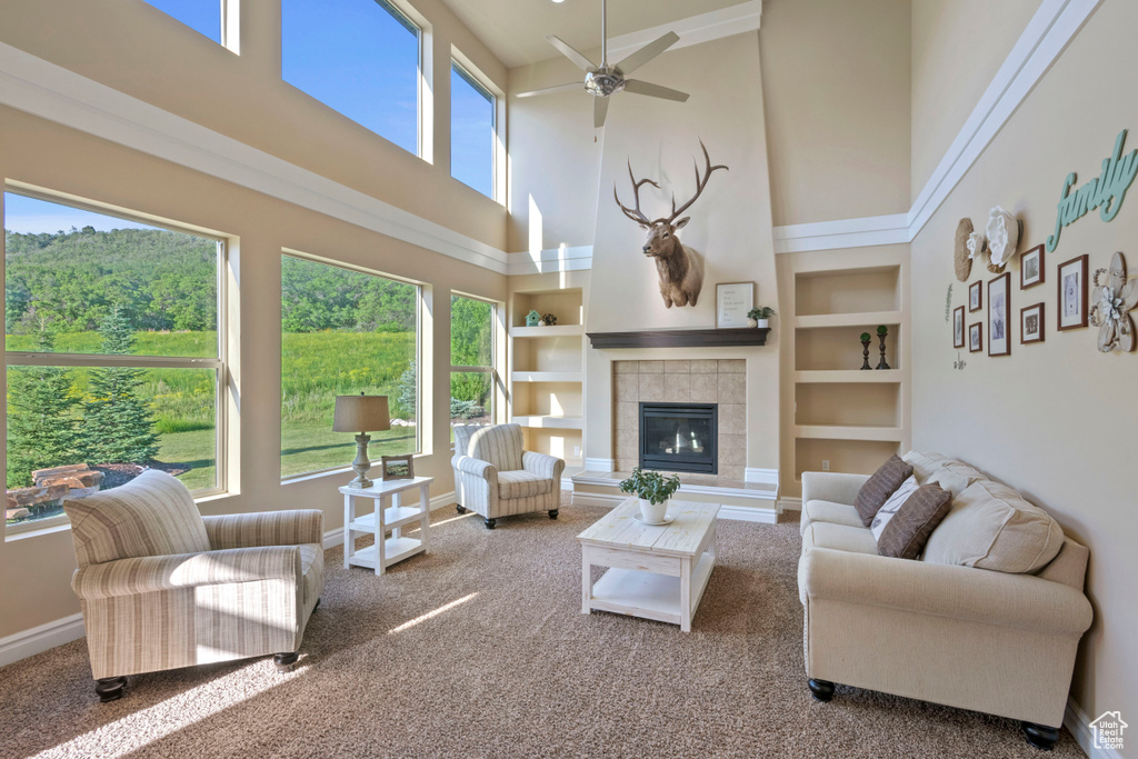 Living room featuring a towering ceiling, carpet flooring, baseboards, a ceiling fan, and a tiled fireplace