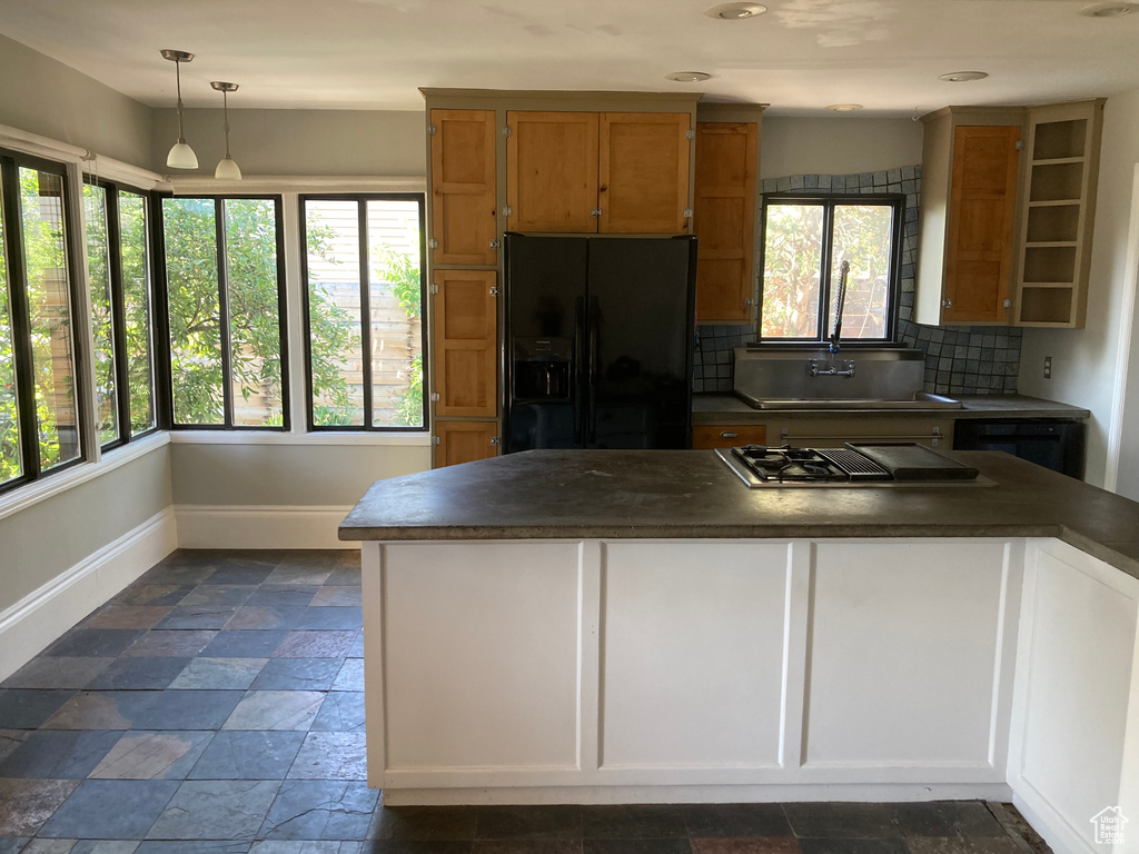 Kitchen with black refrigerator with ice dispenser, stovetop with downdraft, dark countertops, and healthy amount of natural light