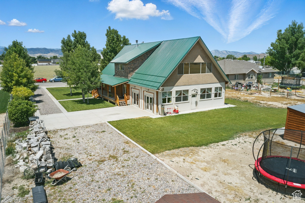 Rear view of property with a trampoline, a mountain view, a lawn, an attached garage, and driveway