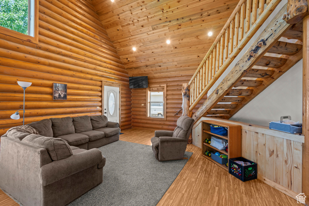 Living area with plenty of natural light, high vaulted ceiling, log walls, wood finished floors, and wooden ceiling