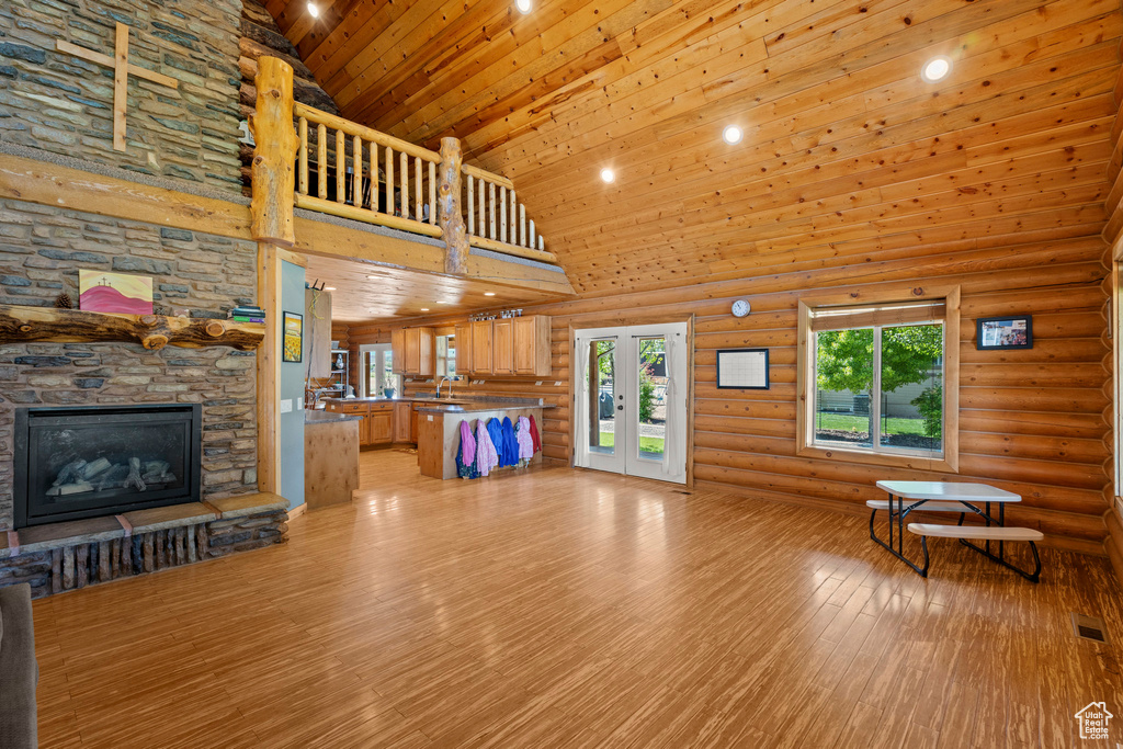 Unfurnished living room featuring high vaulted ceiling, light wood finished floors, a fireplace, and log walls