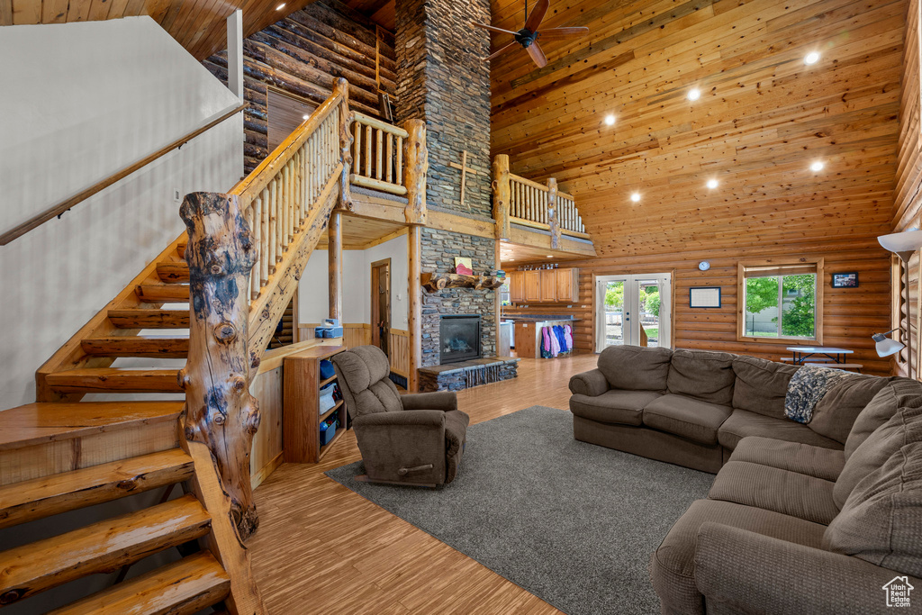 Living room featuring a high ceiling, wood ceiling, log walls, wood finished floors, and a stone fireplace