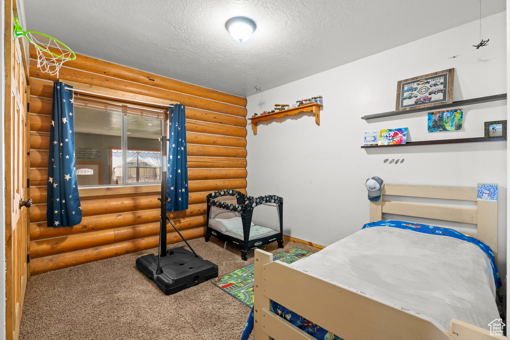 Bedroom featuring log walls, a textured ceiling, and carpet floors